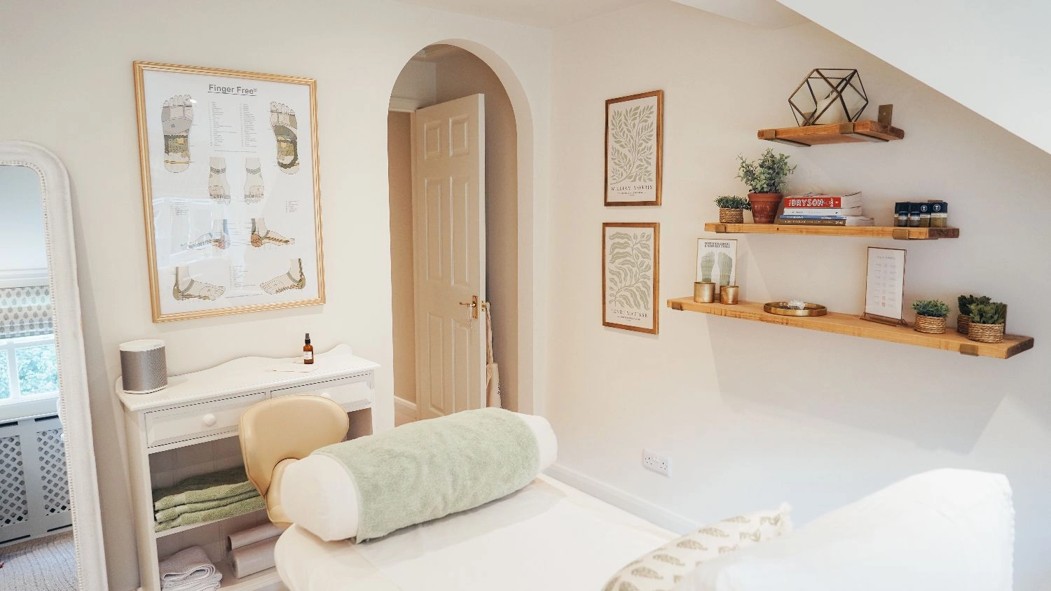 Rutland Reflexology treatment room with posters, wooden shelves with items on, door, and treatment bed